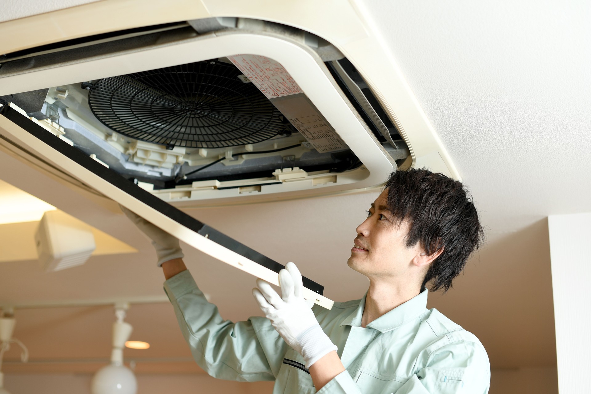 Asian male worker inspecting the air conditioner mounted on the ceiling